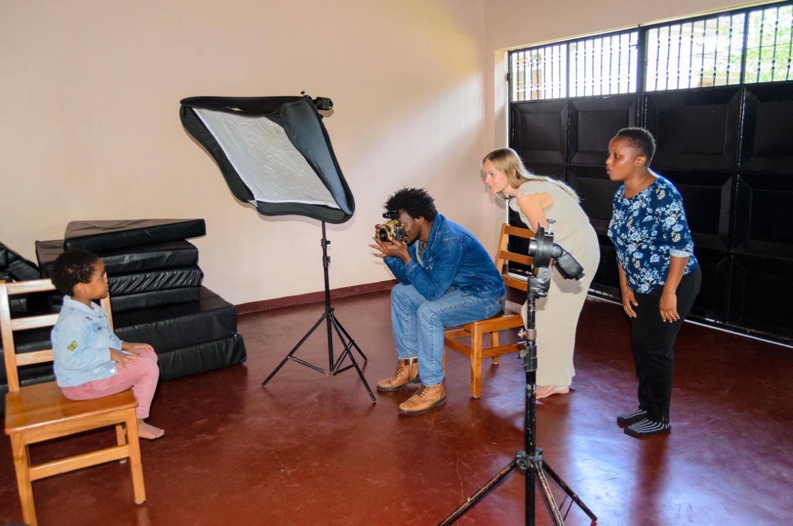 Mirambo Paul photographs a child with two women behind him watching closely.
