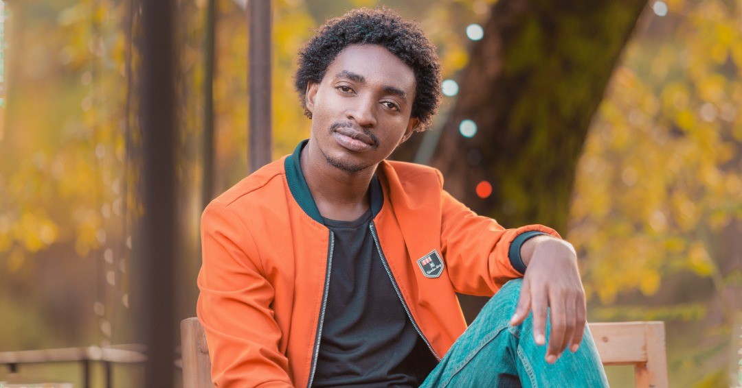A picture of Mirambo Paul sitting on table wearing an orange jacket.